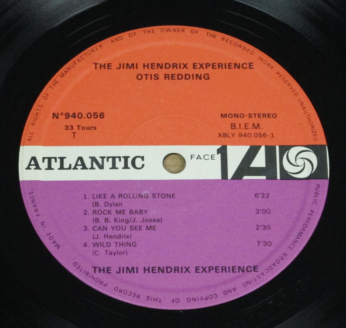 A close-up of a vinyl record label for 'The Jimi Hendrix Experience / Otis Redding' album, released by Atlantic Records. The label features a two-tone color scheme with an orange upper half and a purple lower half. The record information includes catalog number N°940.056, the recording format as mono-stereo, and the B.I.E.M. rights society mark. Listed tracks on this side include 'Like a Rolling Stone' (Bob Dylan), 'Rock Me Baby' (B.B. King / J. Josea), 'Can You See Me' (Jimi Hendrix), and 'Wild Thing' (C. Taylor). The classic Atlantic Records logo is prominently displayed, reinforcing the album’s historical significance in rock and soul music.